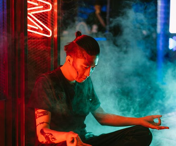 Serene person sitting in a meditative pose surrounded by neon light